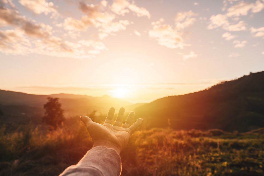 Young,Man,Hand,Reaching,For,The,Mountains,During,Sunset,And