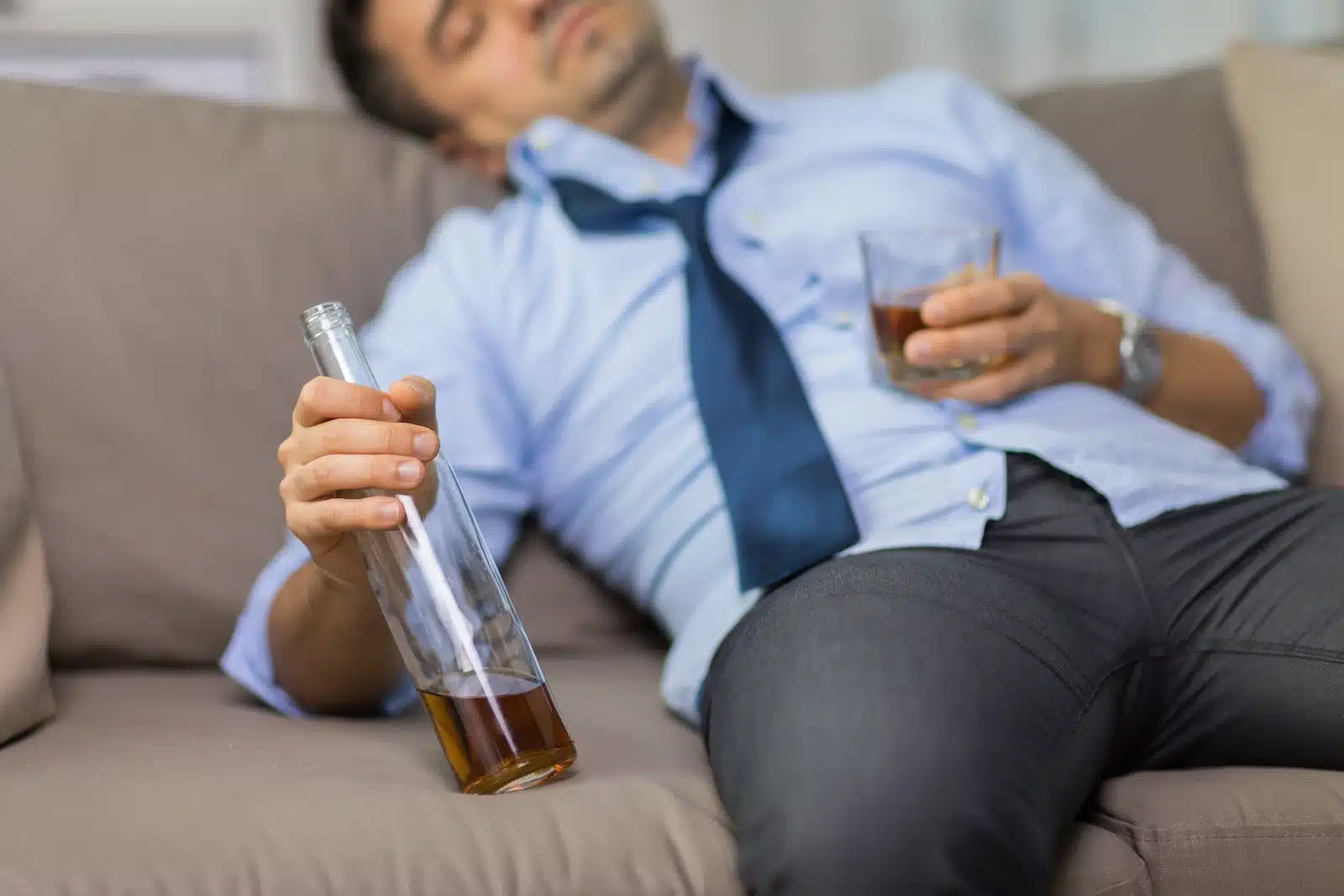 man on sofa holding bottle of alcohol and glass of alcohol